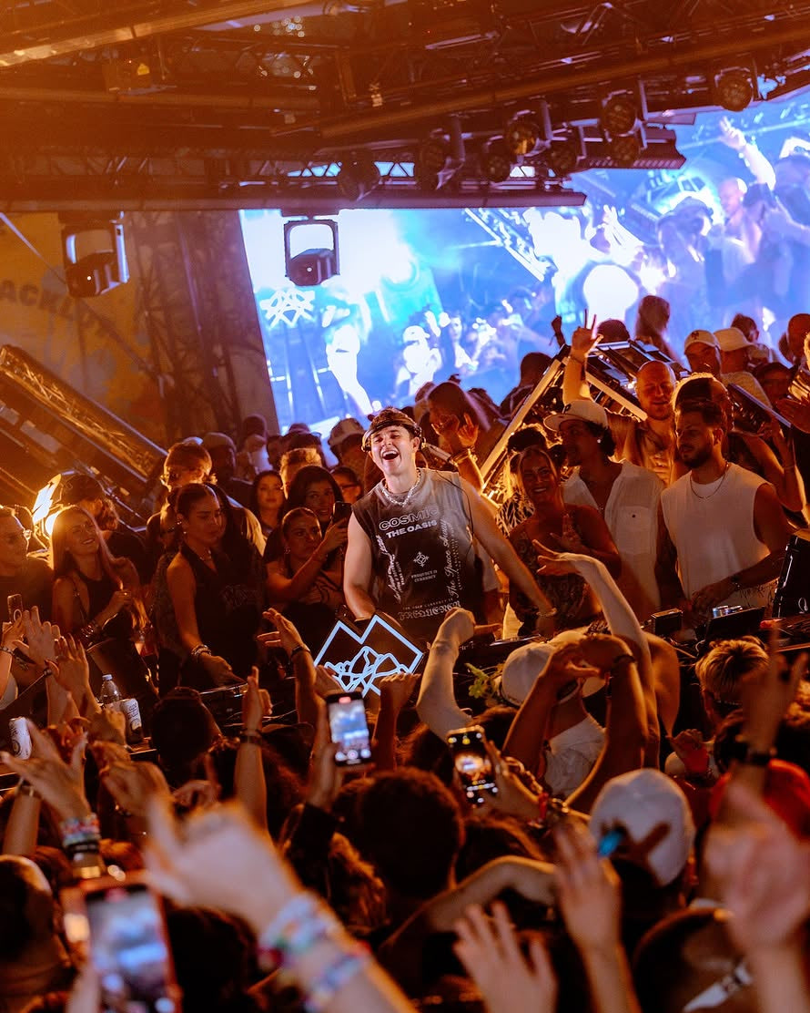 Live concert with a performer on stage and audience members raising hands and holding up phones to the tank top