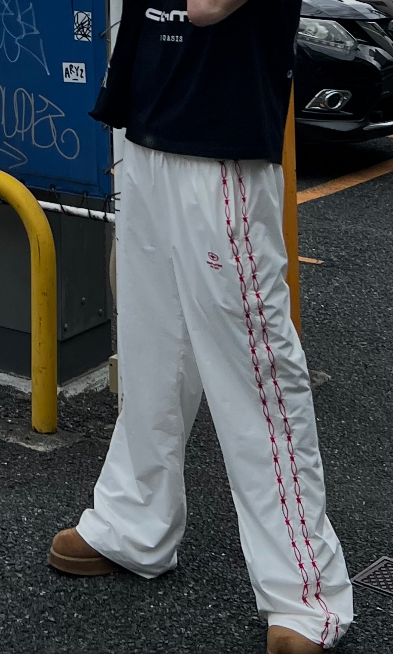 Person wearing white pants with red stitching on a street.